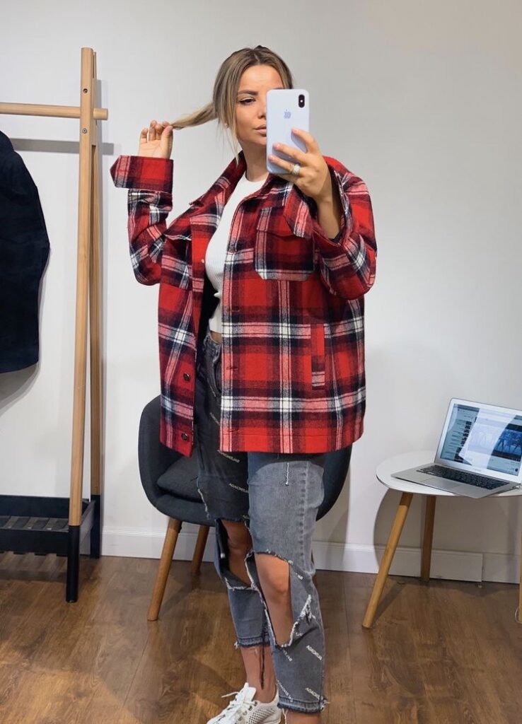 a girl taking a mirror selfie. a girl with a red soft plaid jacket. a girl with white sneakers on. a girl in her room. a girl in front of a big mirror.